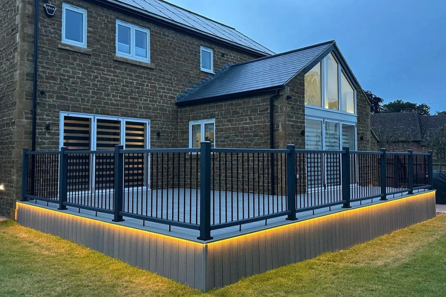 modern house with a composite deck, balustrade, and lighting at dusk