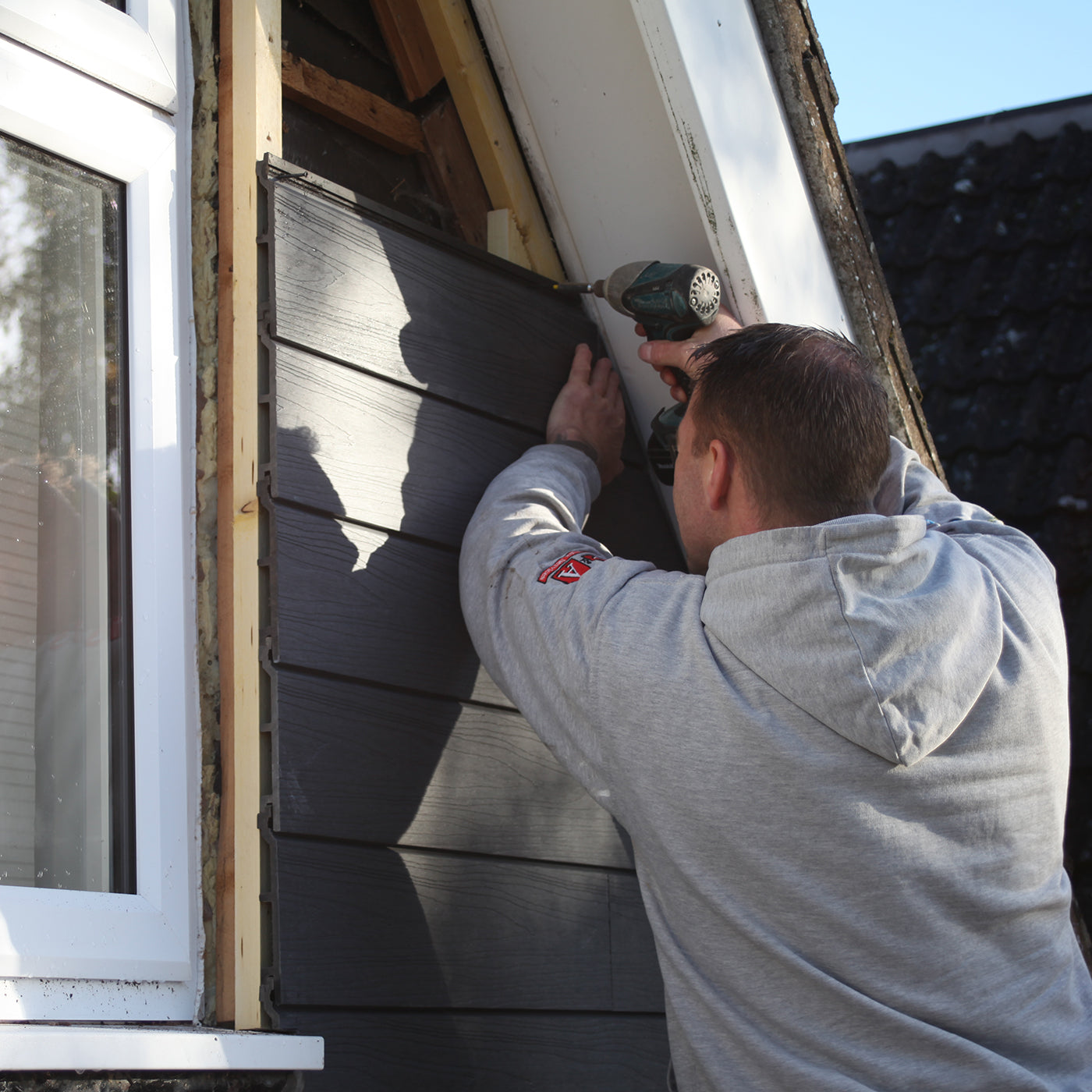 A tradesperson installing grey woodgrain composite cladding on a house exterior, representing the neotimber approved installer program.