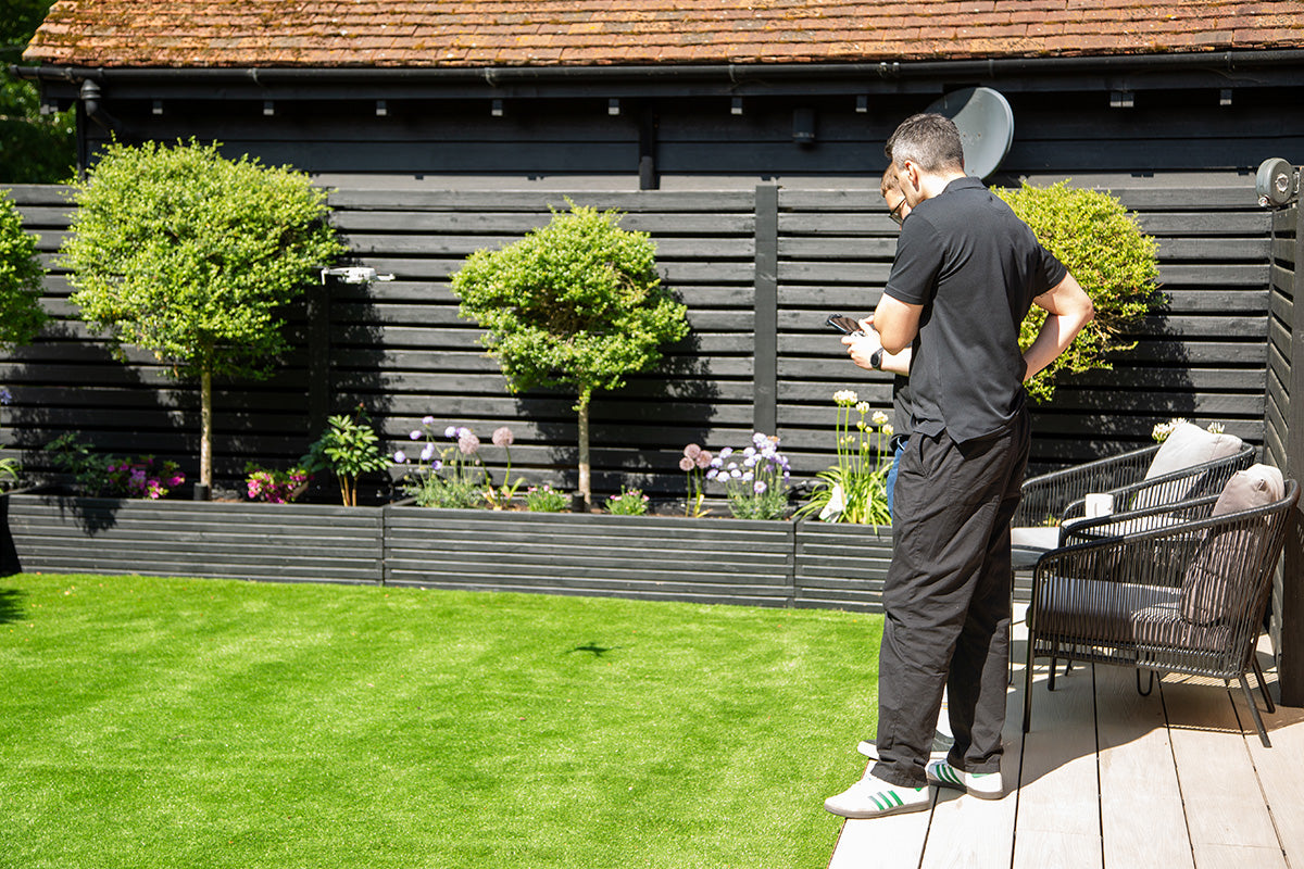 men standing on a composite deck in a garden with a black wooden building and greenery in the background